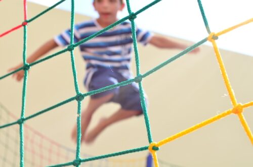 child jumping behind colorful net